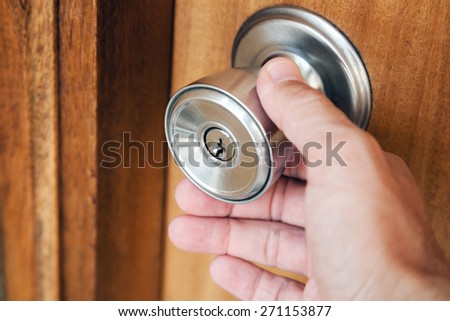 Male hand opening shining metal door handle in closed wooden door, photo with selective focus and shallow DOF
