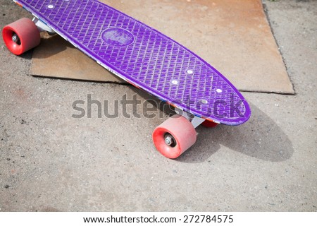 Small size modern purple plastic skateboard stands on an asphalt urban pavement