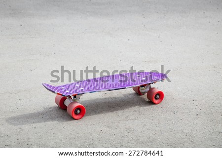 Small size modern purple plastic skateboard stands on an empty urban asphalt road