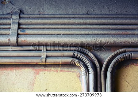 Abstract industrial background, group of bent vintage electrical conduits mounted on a concrete wall.  Old style toned, instagram photo filter effect