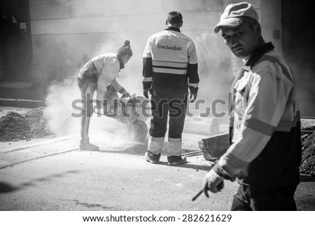 Saint-Petersburg, Russia - May 23, 2015: men at work, urban road under construction, sawing of roadside border stones, black and white photo with selective focus on the saw and shallow DOF