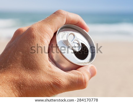 Aluminum can of beer in male hand with blurred beach and sea on a background