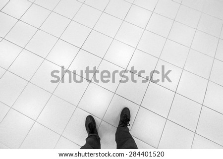 Male feet stand on office floor with white shining square tiling