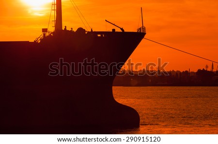 Big industrial cargo ship bow silhouette in bright orange sunset sun light, Varna harbor, Bulgaria. Photo with natural lens flare effect