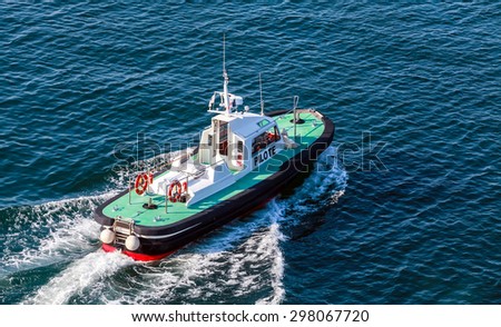 Small pilot boat with green deck and black hull is underway on a sea water