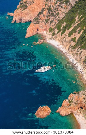 Luxury white pleasure yacht anchored near rocky beach of Corsica island, vertical photo, birds eye view