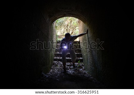 Young man with a flashlight enters the stone tunnel and looks inside with attention and fear