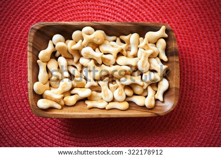 Small salty crackers in shape of fish lay in a wooden bowl on the table with red decorative napkin. Selective focus with shallow DOF