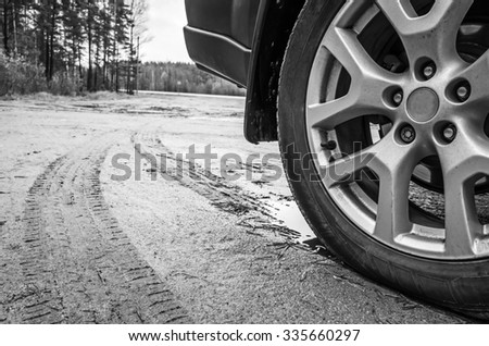 Car wheel with light alloy disc on dirty country road, close up black and white photo