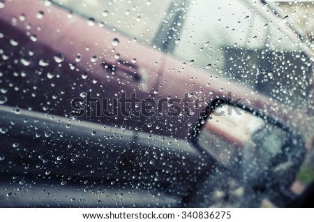 Wet car window with raindrops and a mirror behind. Close-up photo with selective focus and shallow DOF, vintage tonal correction photo filter effect