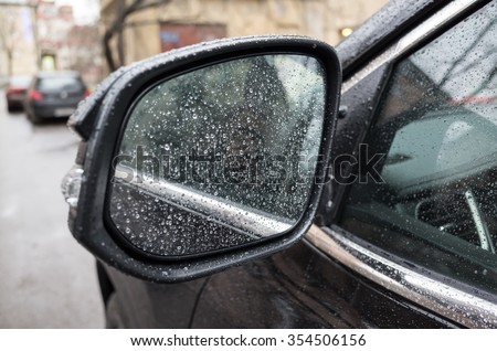 Wet black shining car mirror with raindrops. Closeup photo with selective focus and shallow DOF