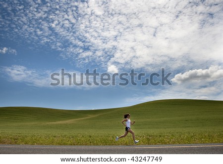 A woman running down a road with green hills and blue sky in the distance