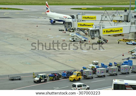 SCHWECHAT, AUSTRIA - MAY 30: Airplane A 320 on passenger boarding bridge, equipment and cargo containers on Vienna airport, on May 30, 2015 in Schwechat, Austria