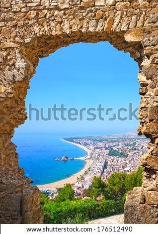 View of Spanish beach through a stone door of the St. John Castle of resort town Blanes in summertime. Costa Brava, Catalonia, Spain