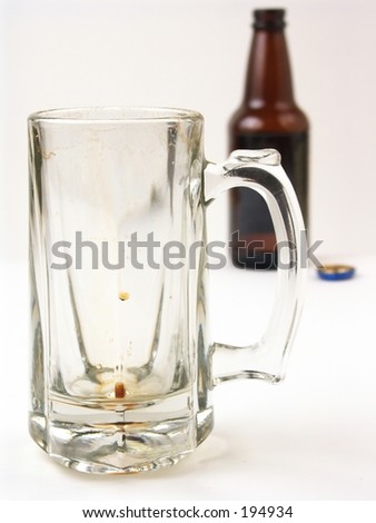 An empty, but recently used beer mug with a beer bottle in the background.