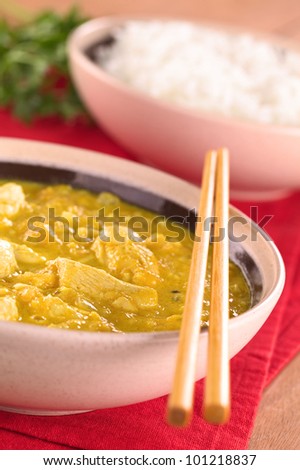 Indian chicken-mango curry dish in bowl with rice in the back (Selective Focus, Focus on the chicken one third into the bowl)
