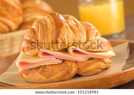 Fresh croissant with ham and cheese on rustic wooden plate with bread basket and orange juice in the back (Selective Focus, Focus on the ham and cheese slices)