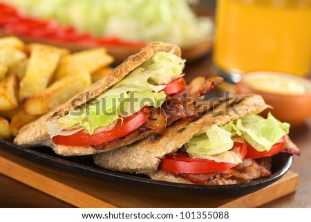 Fresh homemade BLT (bacon lettuce and tomato) wholewheat pita sandwich with French fries on metallic plate with mayonnaise and juice (Selective Focus, Focus on the front of the two pita stuffings)