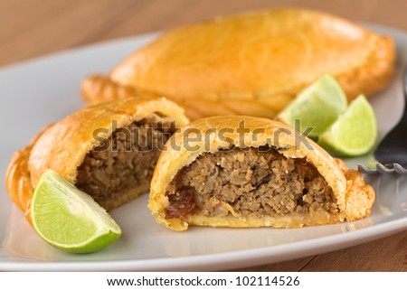 Peruvian snack called Empanada (pie) filled with ground beef meat, onion, raisin on plate with limes (Selective Focus, Focus on the empanada stuffing in the front)