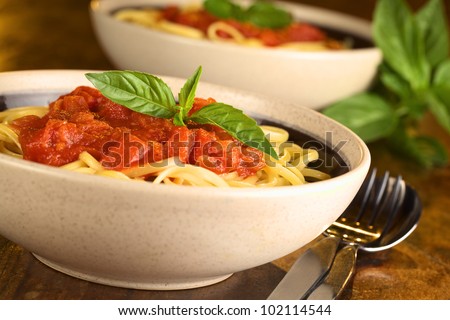 Spaghetti with tomato sauce garnished with a fresh basil leaf served in a bowl (Selective Focus, Focus on the basil leaf in the front)