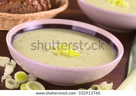 Two bowls full of fresh homemade leek soup with a basket of wholewheat bread in the back (Selective Focus, Focus on the leek rings on the top of the soup)