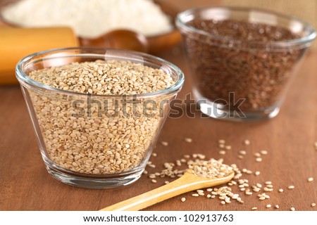 Sesame seeds in glass bowl with flax seeds and flour in the back (Selective Focus, Focus one third into the sesame seeds in the bowl)