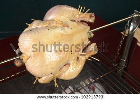 Whole chicken being grilled on spit over a charcoal barbecue (Selective Focus, Focus on the front of the chicken)