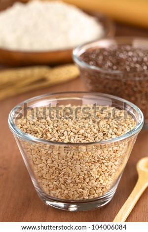 Sesame seeds in glass bowl with flax seeds and flour in the back (Selective Focus, Focus one third into the sesame seeds)
