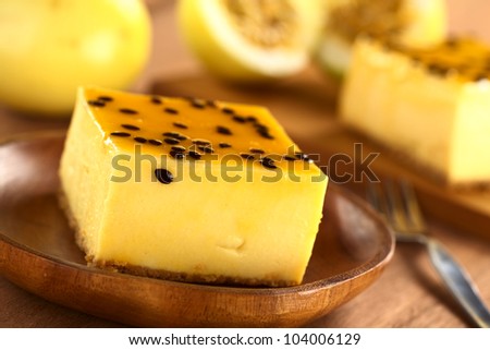 Fresh passion fruit cheesecake dessert on wooden plate with another piece of cake and yellow passion fruit in the back (Selective Focus, Focus on the upper left edge of the cake)