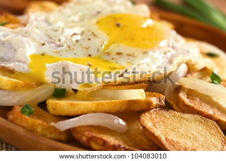 Egg yolk of fried egg running down on crispy fried potato slices with fried onion and scallion (Selective Focus, Focus on the front of the running down egg yolk)