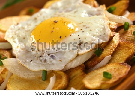 Fresh homemade fried egg with ground pepper on crispy fried potato slices with fried onion and scallion (Selective Focus, Focus on the front of the egg yolk)