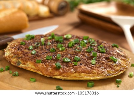Fresh homemade Spanish tortilla (omelette with potatoes) with green onion on top and bread in the back (Selective Focus, Focus one third onto the tortilla)