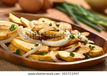 Fresh homemade crispy fried potato slices with fried onion and scallion on wooden plate (Selective Focus, Focus on the front of the onion slice on the top)