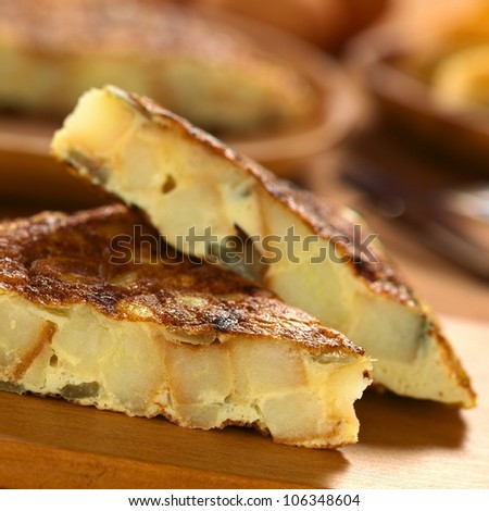 Fresh homemade Spanish tortilla (omelet with potatoes and onions) slices on wooden cutting board (Selective Focus, Focus on the front upper edge of the lower tortilla slice)