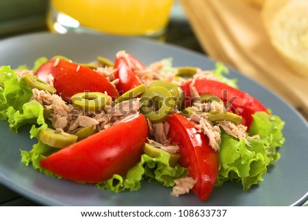Fresh tuna, tomato and green olive salad served on lettuce leaf on blue plate with juice in the back (Selective Focus, Focus on the front of the olive in the middle of the salad)