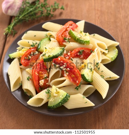 Vegetarian penne pasta dish with baked zucchini and tomato spiced with thyme and garlic (Selective Focus, Focus on the tomato slices in the lower part of the dish)