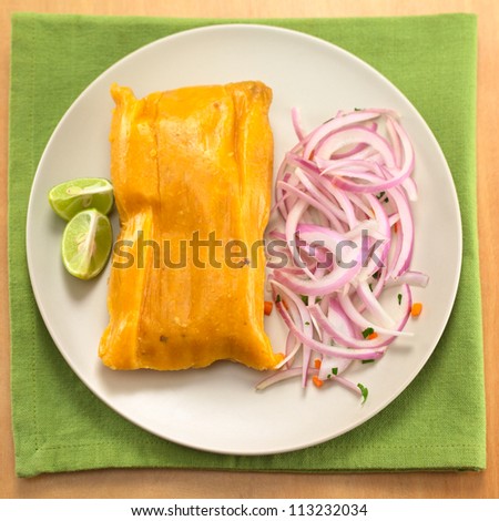 Peruvian tamale (traditionally eaten for breakfast on Sundays) made of corn and chicken and served with salsa criolla (onion salad) and limes (Selective Focus, Focus on the top of the tamale)