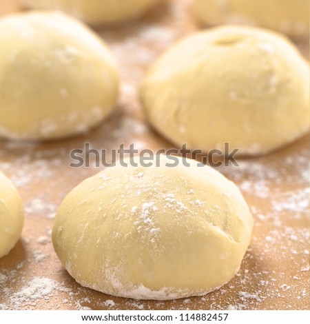 Small balls of fresh homemade pizza dough on floured wooden board  (Selective Focus, Focus one third into the first pizza dough)