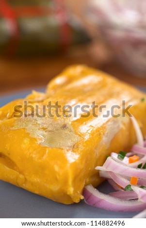 Peruvian tamale (traditionally eaten for breakfast on Sundays) made of corn and chicken and served with salsa criolla (onion salad) (Selective Focus, Focus one third into the tamale)