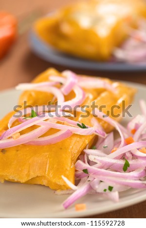 Peruvian tamales (traditionally eaten for breakfast on Sundays) made of corn and chicken with salsa criolla (onion salad) (Selective Focus, Focus on the front of the onion salad on top of the tamale)