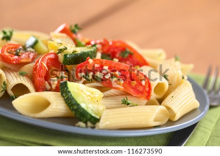 Vegetarian penne pasta dish with baked zucchini and tomato spiced with thyme and garlic (Selective Focus, Focus on the front of the tomato slice one third into the dish)