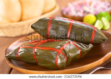 Peruvian tamales wrapped in banana leaves. Inside is a corn-based dough with meat, which are traditionally eaten for breakfast on Sundays (Selective Focus, Focus on the front of the upper tamale)