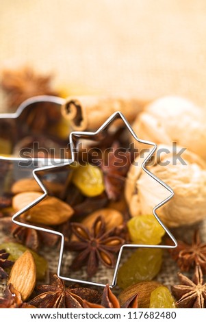 Christmas tree cookie cutter on baking ingredients (walnut, cinnamon, anise, raisin,sultana and almond) (Selective Focus, Focus on the cookie cutter)