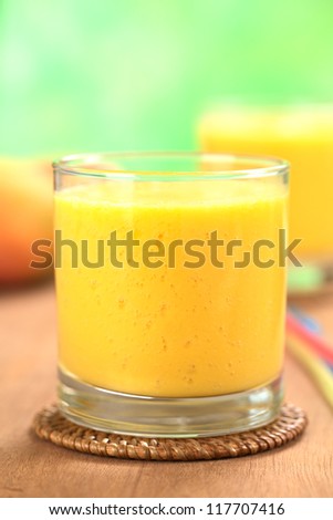 Fresh homemade mango juice in glass with another juice and mango fruits in the back (Selective Focus, Focus on the front upper part of the drink)