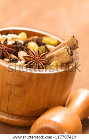 Baking ingredients such as star anise, clove, cinnamon, almond, raisin, sultana and walnut in wooden mortar with pestle in front (Selective Focus, Focus on the middle of the star anise in the front)