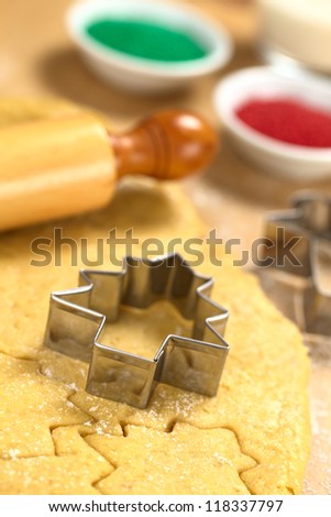 Baking Christmas Cookies: Cookie cutter on rolled out sugar or butter cookie dough with rolling pin and colorful sprinkles in the back (Selective Focus, Focus on the lower edge of the cookie cutter)