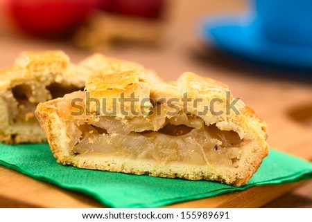 Half apple pie with lattice crust on green napkin on wooden board, with a blue cup, apples and cinnamon sticks in the back  (Selective Focus, Focus on the front of the filling of the pie)
