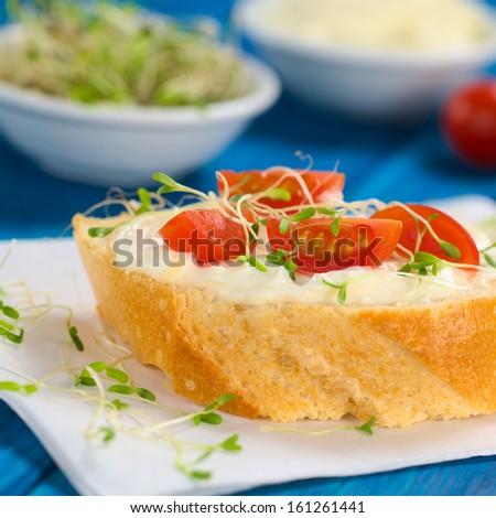Baguette slice spread with cream cheese, with cherry tomato and alfalfa sprouts on top served on sandwich paper (Selective Focus, Focus on the front of the first tomato pieces)