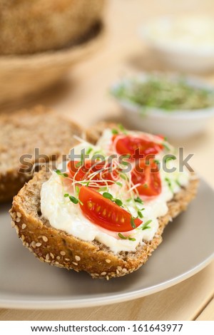Wholewheat bread spread with cream cheese, with cherry tomato and alfalfa sprouts on top served on plate (Selective Focus, Focus on the tomato in the front)