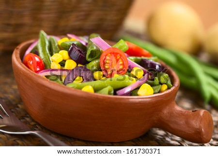 Fresh colorful vegetarian salad made of green beans, cherry tomatoes, sweet corn, black olives and red onions in rustic bowl (Selective Focus, Focus on the tomato in the middle)